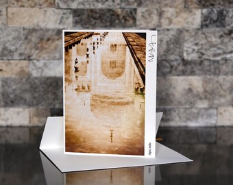 May include: A sepia-toned greeting card featuring a photograph of the Taj Mahal reflected in water. The card is propped up on a white base, with the text "Agra, India" visible. The background is a textured stone wall.
