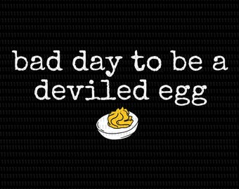 May include: Black background with white text that reads "bad day to be a deviled egg." Below the text is a cartoon illustration of a deviled egg with yellow filling. The image is a humorous food-themed design.