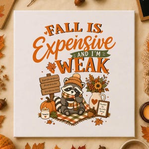 May include: A square white canvas print featuring a cartoon raccoon wearing a beanie and scarf, holding a coffee cup. The text reads FALL IS Expensive AND I'M WEAK. Includes a pumpkin, a wooden sign, a vase of flowers, and an acorn on a plaid blanket.