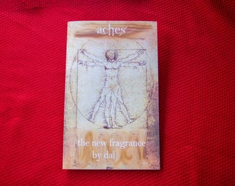 May include: A rectangular card with the word "aches" at the top and the text "the new fragrance by dal" at the bottom. The card features a sepia-toned illustration of a human figure within a circle, reminiscent of the Vitruvian Man, set against a red background.