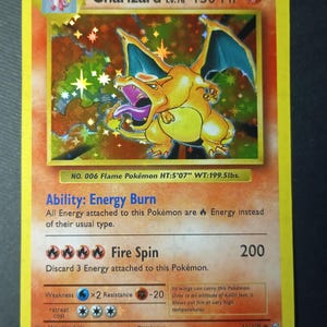 Op de afbeelding: Een Charizard Pokémon-verzamelkaart. De kaart toont een holografische afbeelding van Charizard, een geel en oranje draakachtig wezen met blauwe vleugels. De kaart heeft tekst, waaronder "Charizard Lv.76 150 HP". De kaart is 170 cm lang en weegt 90,5 kg.