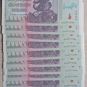 Op de afbeelding: Een stapel Zimbabwaanse bankbiljetten van honderd quintiljoen dollar. Elk biljet toont de tekst "ONE HUNDRED QUINTILLION DOLLARS" en een afbeelding van balancerende rotsen en een neushoorn. De biljetten zijn groen, paars en wit.
