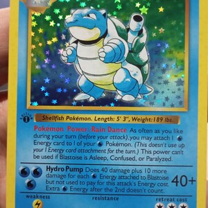 Pode incluir: Carta Pokémon holográfica Blastoise. A carta apresenta uma criatura azul e branca semelhante a uma tartaruga com dois canhões nas costas. O texto da carta inclui "Blastoise", "Hydro Pump" e "LV.52 #9". É uma carta Fase 2.