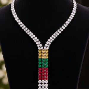 Op de afbeelding: Een Y-vormige ketting met twee strengen van heldere ronde stenen die samenkomen in een centrale verticale hanger. De hanger bestaat uit drie rijen gele, groene, rode en heldere stenen gerangschikt in kleurblokken.