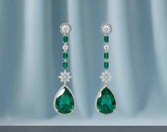 May include: Elegant drop earrings featuring pear-shaped emeralds, accented with diamonds and a floral design. The earrings have a total length of approximately 3 inches.
