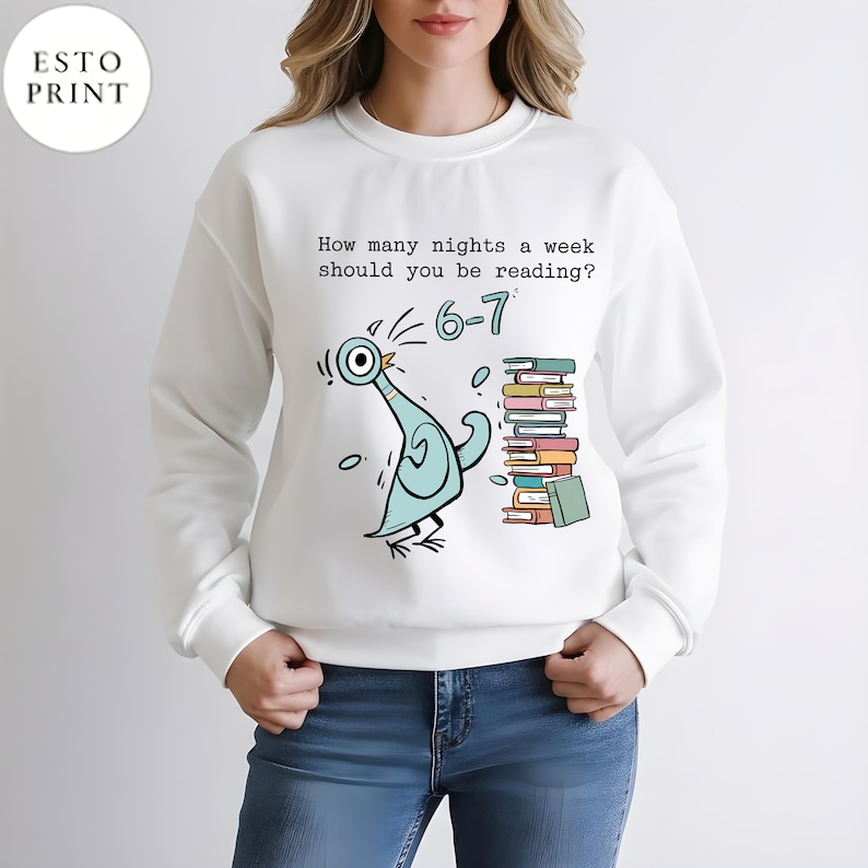 K&ouml;nnte beinhalten: Wei&szlig;es Sweatshirt mit einer Cartoon-Tauben-Illustration und dem Text "How many nights a week should you be reading? 6-7". Die Taube ist hellblau mit schwarzen Akzenten, und ein Stapel B&uuml;cher befindet sich rechts.
