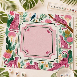 May include: A square mahjong mat featuring a pink central area with decorative borders, surrounded by a jungle-themed print of pink leopards, green foliage, cacti, and a blue bird. The mat includes printed text instructions for Charleston play.