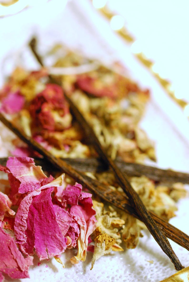 May include: Close-up of a collection of natural ingredients, including pink rose petals, dried flowers, and dark brown vanilla beans. The arrangement is artfully composed, suggesting a focus on aromatherapy or natural beauty products.