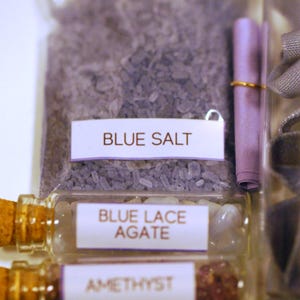 May include: Close-up of various small glass bottles and a clear plastic bag filled with crystals and stones. The bottles contain Blue Lace Agate and Amethyst. The bag is labeled "BLUE SALT".