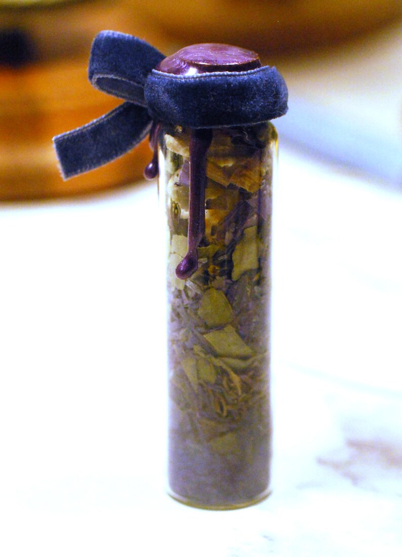 May include: A small glass bottle filled with dried herbs and a dark purple wax seal. The bottle is topped with a dark blue velvet ribbon tied in a bow. The wax seal drips down the side of the bottle.