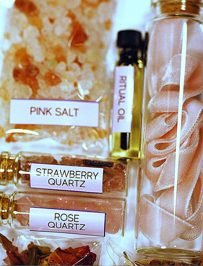 May include: An assortment of self-care products, including pink salt, strawberry quartz, rose quartz, and ritual oil. The items are packaged in clear containers and bags, with labels identifying each product. A glass jar contains pink ribbon.