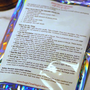 May include: A holographic package with text instructions for a spell jar. The text includes steps for adding ingredients like pink salt, quartz, rose petals, and vanilla bean shards. The package has a metallic, iridescent sheen.
