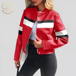 Könnte beinhalten: Rote Kunstlederjacke mit schwarzen und weißen Streifen an Ärmeln und Brust. Die Jacke hat einen Stehkragen, einen Reißverschluss und eine taillierte Passform. Das Logo von The Shop Vana Apparel ist sichtbar.