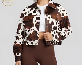 May include: Cropped cow print jacket with brown and white spots. The jacket has a collared neckline, two front pockets, and brown accents on the collar and pockets. The Shop View Apparel logo is in the upper left corner.