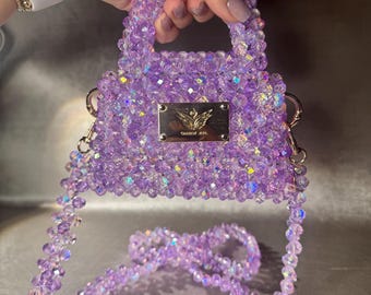 Bolsa pequena de vidro roxo com cristais bordados à mão, alça transversal com detalhes em dourado e aplicações de miçangas.