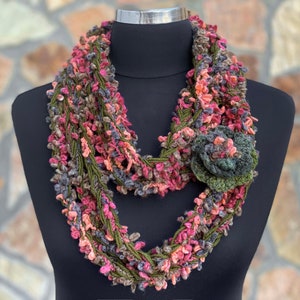 Può includere: Un'infinita sciarpa all'uncinetto in tonalità rosa, verde e grigio con un fiocco di uncinetto abbinato.
