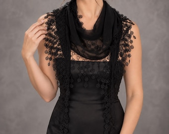 May include: A black scarf featuring a sheer fabric centre and intricate lace borders adorned with circular floral patterns. The lace trim extends along the edges, creating a delicate, dangling fringe effect that drapes over the shoulders and chest.