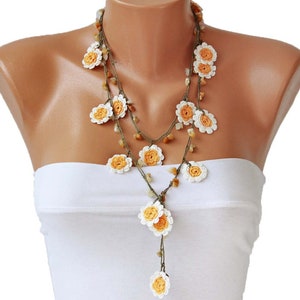 May include: A long, layered necklace with crocheted flowers in white and orange. The necklace is made of brown cord and has small, round beads.