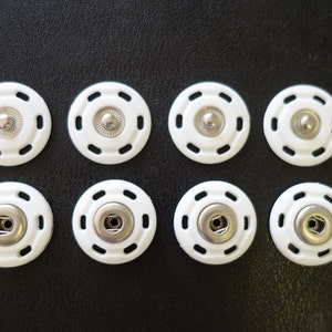 May include: Eight white plastic snap fasteners with silver metal centers. The fasteners are arranged in two rows of four.