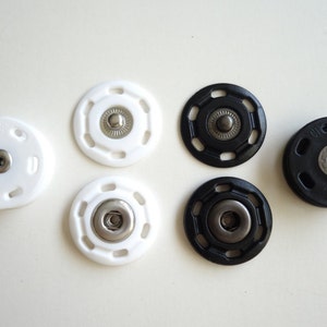 May include: Assortment of black and white plastic snap fasteners. The fasteners have a metal center and are designed for sewing onto fabric.
