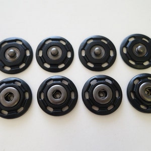 May include: Eight black plastic snap fasteners with a silver metal center. The fasteners are arranged in two rows of four.