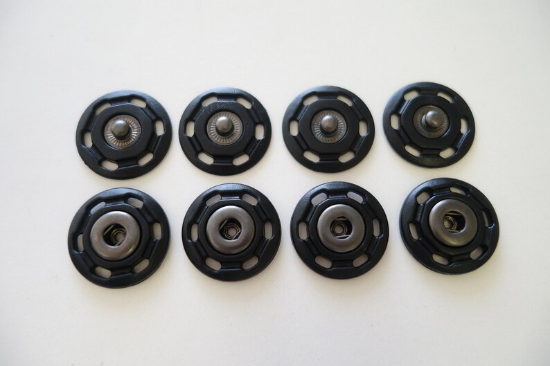May include: Eight black plastic snap fasteners with a silver metal center. The fasteners are arranged in two rows of four.