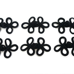 May include: Six black Chinese knot buttons, also known as frog closures, are arranged in two rows of three. Each button is made of a single piece of black cord that is tied into a decorative knot.