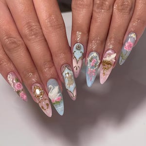 Puede incluir: Un conjunto de uñas acrílicas largas y puntiagudas con intrincados diseños en 3D. Cada uña presenta un esquema de color pastel diferente, incluyendo rosa, azul y blanco, con adornos ornamentados como rosas, cisnes y detalles dorados. Las uñas muestran un estilo artístico y caprichoso.