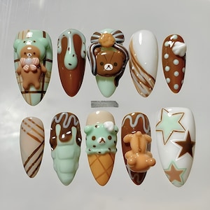 May include: A set of ten almond-shaped press-on nails with a dessert theme. Designs include teddy bears, ice cream cones, and chocolate drips in shades of brown, mint green, and white. Some nails feature star and polka dot patterns.