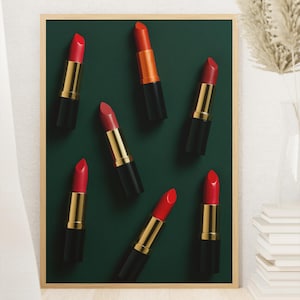 Op de afbeelding: Een ingelijste afbeelding met zeven lippenstiften tegen een donkergroene achtergrond. De lippenstiften zijn in verschillende tinten rood en oranje, met gouden en zwarte hulzen. De afbeelding staat tegen een neutrale muur met een vaas en boeken.