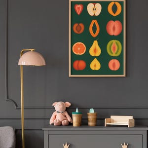 Peut inclure: Une affiche encadr&eacute;e pr&eacute;sentant des illustrations color&eacute;es de divers fruits, dont une fraise, une pomme et un kiwi, sur un fond vert fonc&eacute;. L'affiche est au-dessus d'une commode grise avec des poign&eacute;es en forme de couronne en bois. Un cochon en peluche rose et des tasses en bois sont sur la commode.