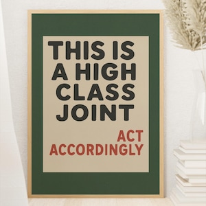 May include: A framed art print with a green border and a tan background. The text reads "THIS IS A HIGH CLASS JOINT" in black, with "ACT ACCORDINGLY" in red. The print is displayed on a white wall.