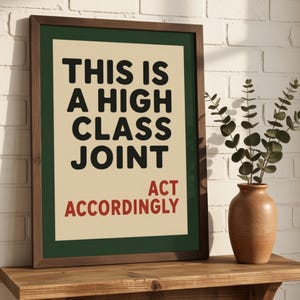 May include: A framed wall art print featuring a cream-colored background with a dark green border. The text reads in bold black letters, THIS IS A HIGH CLASS JOINT, and in smaller red letters below, ACT ACCORDINGLY. The frame is made of dark brown wood.