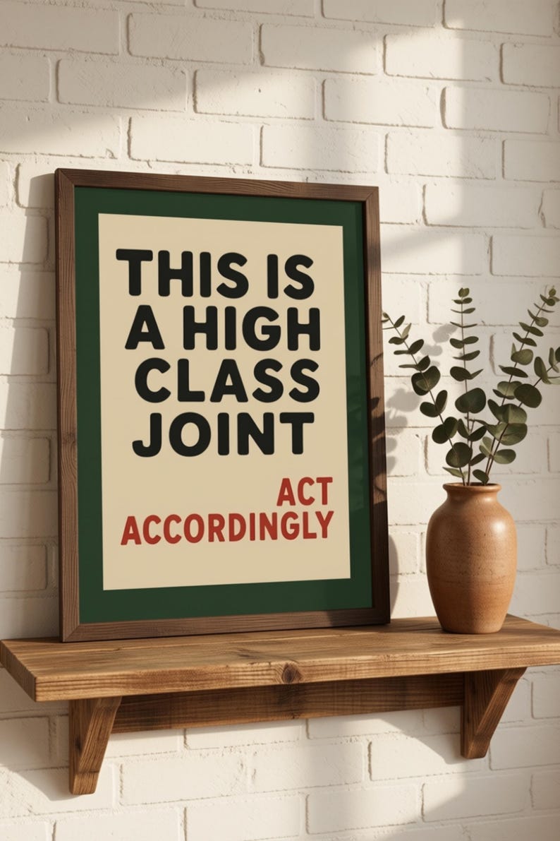 May include: A framed wall art print featuring a cream-colored background with a dark green border. The text reads in bold black letters, THIS IS A HIGH CLASS JOINT, and in smaller red letters below, ACT ACCORDINGLY. The frame is made of dark brown wood.