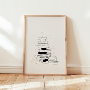 May include: A framed minimalist art print featuring a stack of books. The artwork is a black and white line drawing, with the books in varying sizes and orientations. The frame is a light wood color, and the background is a neutral off-white.