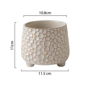 Puede incluir: Maceta de cer&aacute;mica beige con un patr&oacute;n texturizado en forma de panal. La maceta mide 11 cm de alto, 11,5 cm de ancho y 10,8 cm de di&aacute;metro. Tiene tres peque&ntilde;os pies y una amplia abertura.