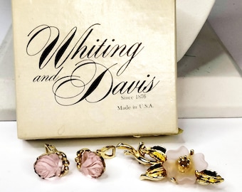 May include: A vintage Whiting and Davis jewellery set, comprising earrings and a brooch. The earrings and brooch showcase a pink floral design with gold-tone metal detailing. The cream-coloured box bears the brand name and "Made in U.S.A."