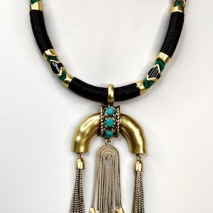 May include: A statement necklace featuring a black cord with gold and green accents. The pendant is a gold-toned arch with turquoise accents and chain tassels. A unique piece of jewelry.