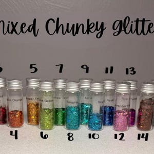 May include: A collection of seventeen small, clear glass vials filled with various colors of chunky glitter, arranged in a row. Each vial is topped with a silver screw cap and labeled with a number from 1 to 17. The text Mixed Chunky glitter is visible.
