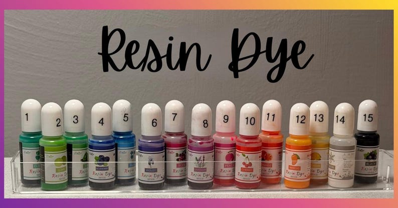 May include: Fifteen small bottles of resin dye arranged in a clear plastic tray. Each bottle features a white cap, a numbered label from 1 to 15, and a colorful graphic representing the pigment shade. The text Resin Dye is printed above.