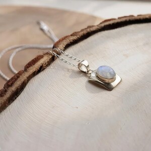 May include: A silver pendant necklace featuring an oval-shaped, iridescent moonstone set in a smooth metal bezel. The pendant is attached to a delicate silver chain, showcasing a polished finish that reflects light across the stone's surface.
