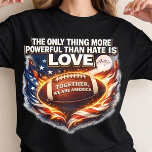 Puede incluir: Camiseta negra con un diseño de fútbol americano con la bandera estadounidense y llamas. El texto dice "THE ONLY THING MORE POWERFUL THAN HATE IS LOVE" y "TOGETHER, WE ARE AMERICA."