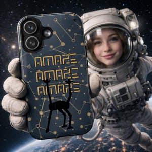 May include: A dark blue phone case with a constellation design and the word "AMAZE" repeated three times in gold. A black silhouette of a creature is below the text. The phone case is held by a person in a spacesuit, with the Earth and stars in the background.