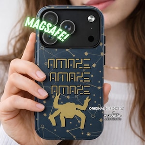 Könnte beinhalten: Eine dunkelblaue Handyhülle mit goldenem Sternbildmuster, dem dreimal wiederholten Text "AMAZE" und einer goldenen Spinnengrafik. Die Hülle enthält einen schwarzen Kamerabereich mit dem grünen Text "MAGSAFE!" und dem Logo "mubiio AESTHETIC".