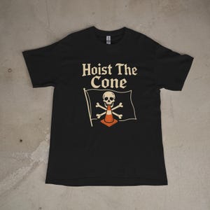 May include: Black t-shirt with the text "Hoist The Cone" above a flag design. The flag features a skull, crossbones, and an orange traffic cone. The shirt is a crew neck style.