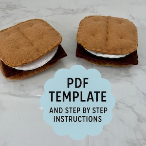 May include: Two felt s'mores, each with a brown graham cracker top and bottom, a white marshmallow, and a dark chocolate layer. The image includes a light blue cloud-shaped graphic with the text "PDF TEMPLATE AND STEP BY STEP INSTRUCTIONS."