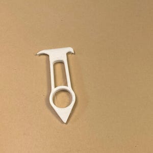 May include: A white, 3D-printed tool with a ring, a handle, and a pointed end. The tool has a unique shape and design, possibly for a specific purpose. The object is set against a neutral background.