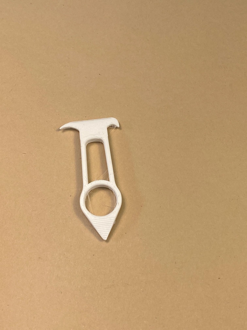 May include: A white, 3D-printed tool with a ring, a handle, and a pointed end. The tool has a unique shape and design, possibly for a specific purpose. The object is set against a neutral background.