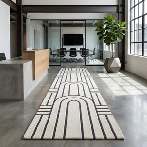 Puede incluir: Una alfombra de pasillo rectangular larga con una base de color crema y un patrón geométrico repetitivo de color gris oscuro que consiste en arcos anidados y líneas horizontales, situada sobre un suelo de hormigón liso.