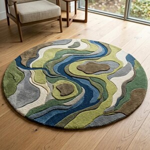 Puede incluir: Una alfombra circular con un diseño inspirado en la topografía, con formas orgánicas fluidas en tonos verde bosque, salvia, azul marino, gris pizarra, crema y marrón tierra, creando una apariencia texturizada y dimensional.